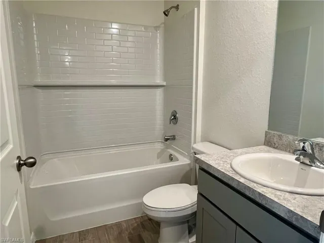 Full bathroom with vanity, a textured wall, wood finished floors, and shower / washtub combination