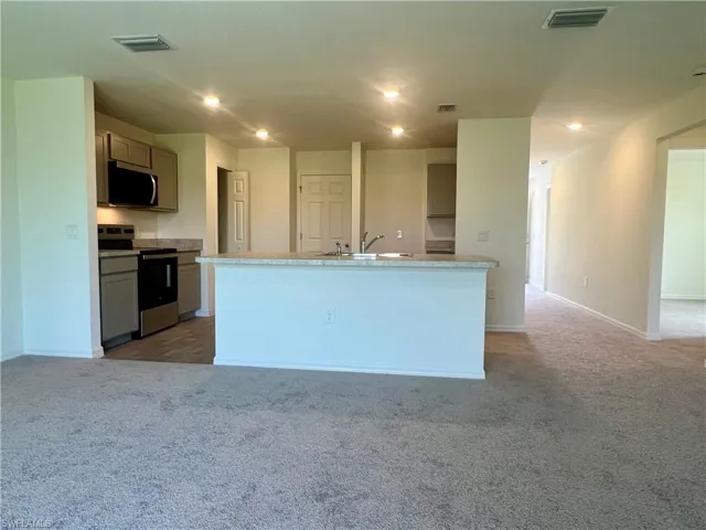 Kitchen with appliances with stainless steel finishes, light colored carpet, an island with sink, recessed lighting, and light countertops