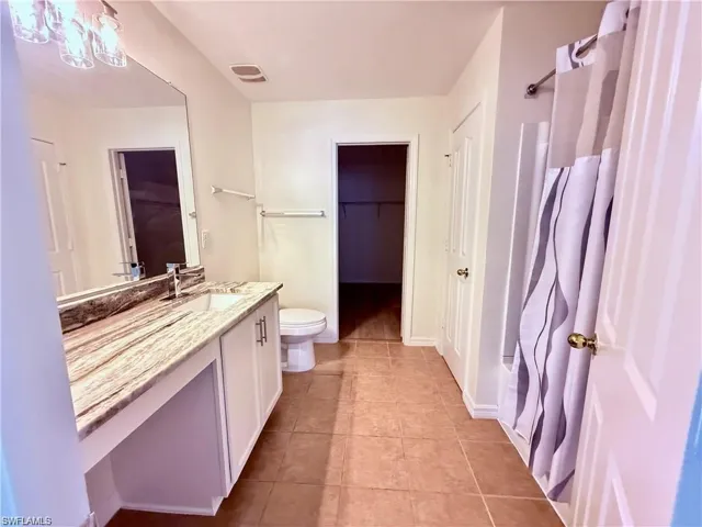 Bathroom with vanity, toilet, a walk in closet, and tile patterned flooring