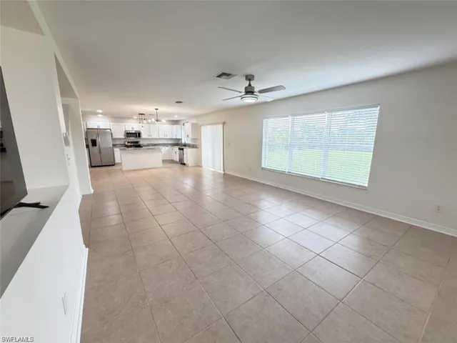 Unfurnished living room featuring light tile patterned floors, a ceiling fan, and baseboards
