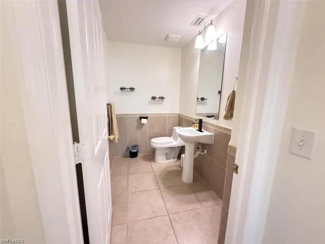 Half bath featuring tile walls, tile patterned floors, a wainscoted wall, and toilet