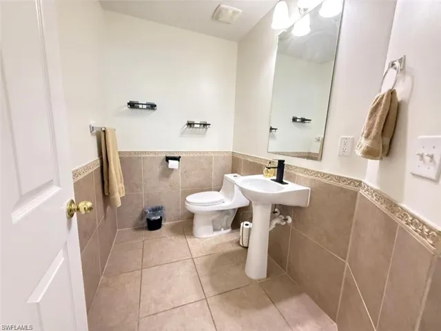 Bathroom featuring tile walls, wainscoting, tile patterned floors, and toilet