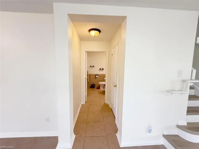Corridor with light tile patterned flooring, stairs, and baseboards