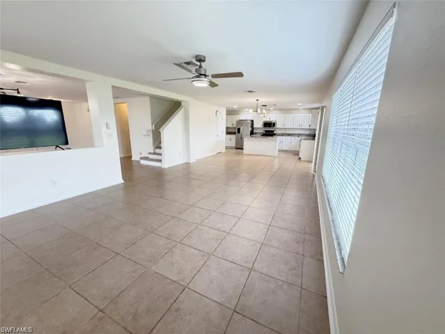 Unfurnished living room with light tile patterned flooring, ceiling fan, stairway, and baseboards