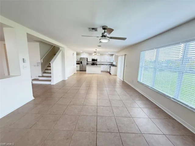 Unfurnished living room with a ceiling fan, light tile patterned floors, stairs, and baseboards