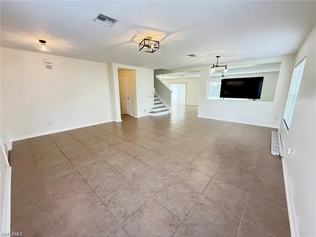 Unfurnished living room featuring stairs, tile patterned floors, and baseboards