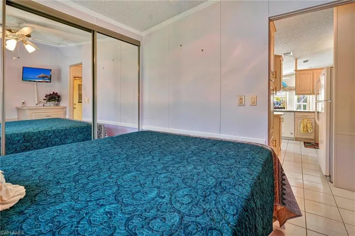 Tiled bedroom featuring white refrigerator, ornamental molding, ceiling fan, and a textured ceiling