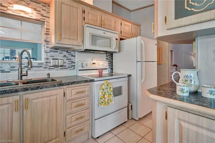 Kitchen featuring tasteful backsplash, white appliances, light brown cabinetry, light tile floors, and sink