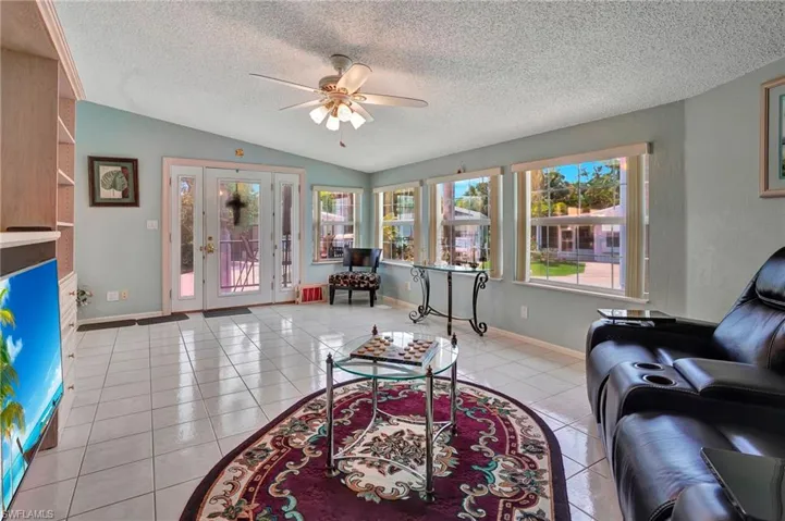 Living room with ceiling fan, a textured ceiling, light tile flooring, and lofted ceiling