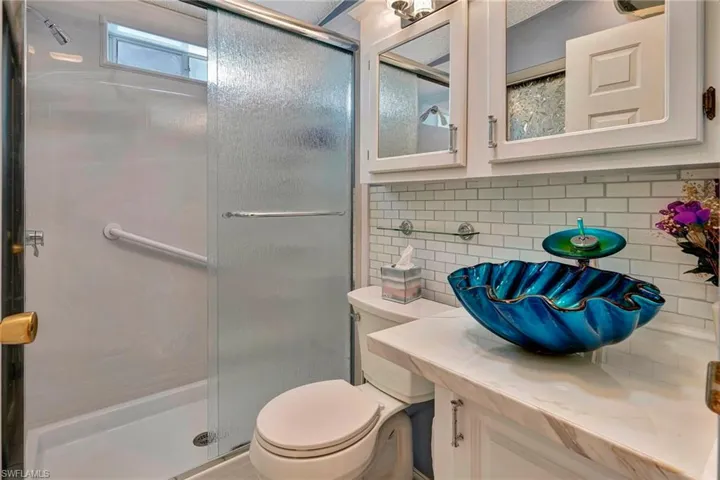 Bathroom featuring an enclosed shower, backsplash, vanity, and toilet
