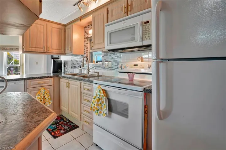 Kitchen featuring light tile flooring, tasteful backsplash, sink, white appliances, and a textured ceiling