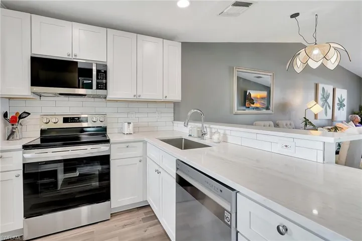 Kitchen featuring lofted ceiling, sink, light hardwood / wood-style floors, white cabinetry, and stainless steel appliances