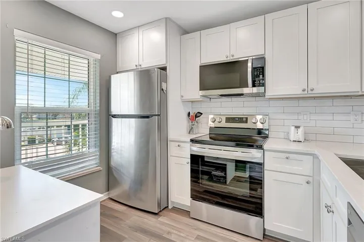 Kitchen featuring white cabinets, backsplash, light wood-type flooring, and stainless steel appliances