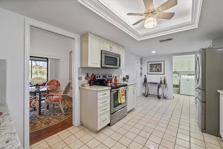 Kitchen featuring stainless steel appliances, ceiling fan, washer / dryer, a tray ceiling, and light tile patterned flooring