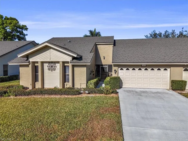 View of front facade featuring a shingled roof, a front lawn, driveway, and stucco siding