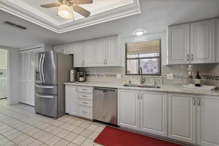 Kitchen featuring white cabinets, light stone countertops, stainless steel appliances, and a tray ceiling