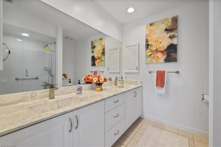 Bathroom featuring double vanity, tiled shower, light tile patterned floors, and recessed lighting
