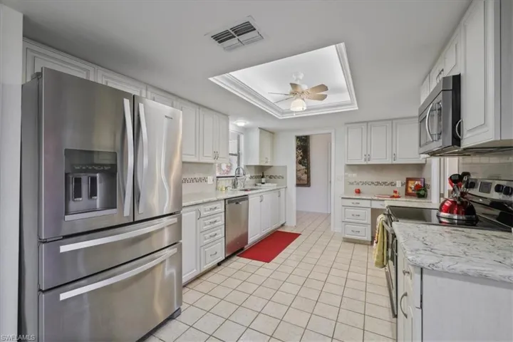 Kitchen with stainless steel appliances, white cabinetry, a ceiling fan, a tray ceiling, and light tile patterned floors