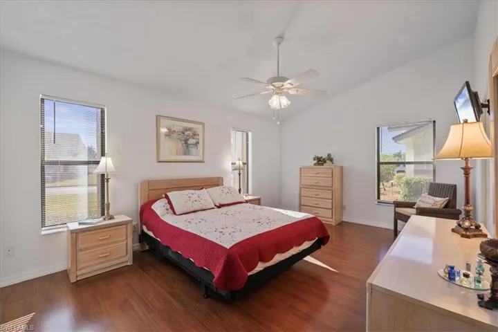 Bedroom featuring dark wood finished floors, vaulted ceiling, a ceiling fan, and multiple windows