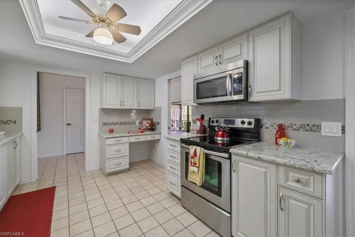 Kitchen with stainless steel appliances, a ceiling fan, white cabinetry, tasteful backsplash, and a raised ceiling