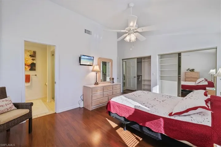 Bedroom with multiple closets, wood finished floors, ceiling fan, and vaulted ceiling