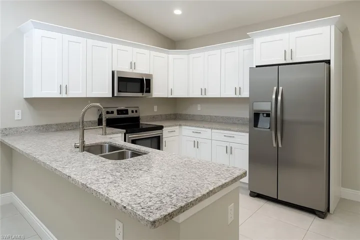Kitchen featuring appliances with stainless steel finishes, white cabinets, light tile patterned floors, a peninsula, and light stone countertops