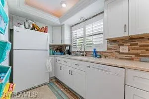 Kitchen with white appliances, white cabinets, a tray ceiling, light countertops, and crown molding