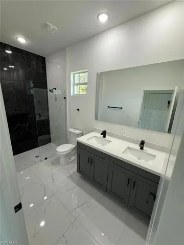 Bathroom with double vanity, a marble finish shower, light marble finish floors, and recessed lighting
