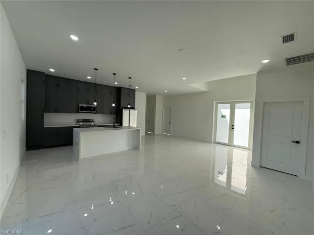 Kitchen with open floor plan, an island with sink, decorative light fixtures, stainless steel appliances, and light marble finish floors