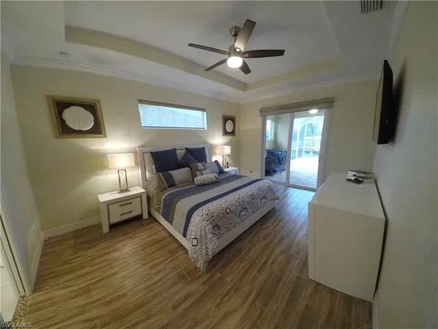 Bedroom with access to outside, a tray ceiling, ceiling fan, crown molding, and wood-type flooring