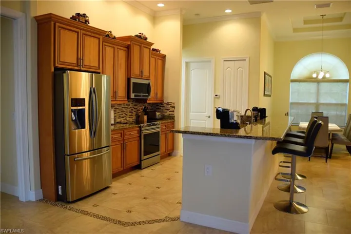 Kitchen with dark stone countertops, a towering ceiling, a chandelier, a kitchen bar, and appliances with stainless steel finishes