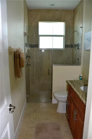 Bathroom featuring tile patterned floors, a shower with door, vanity, and toilet