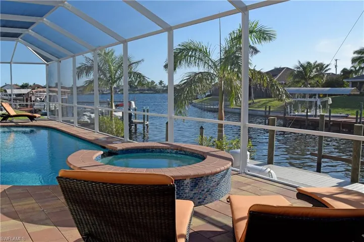 View of swimming pool featuring an in ground hot tub, a dock, a water view, glass enclosure, and a patio area