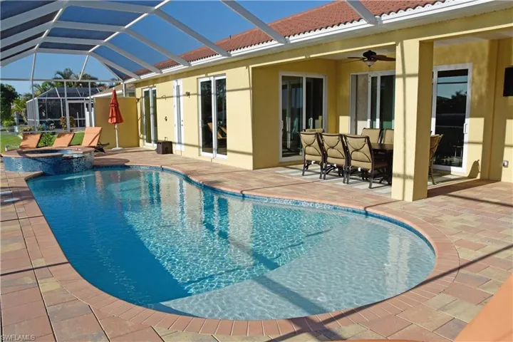 View of swimming pool with glass enclosure, ceiling fan, a patio, and an in ground hot tub