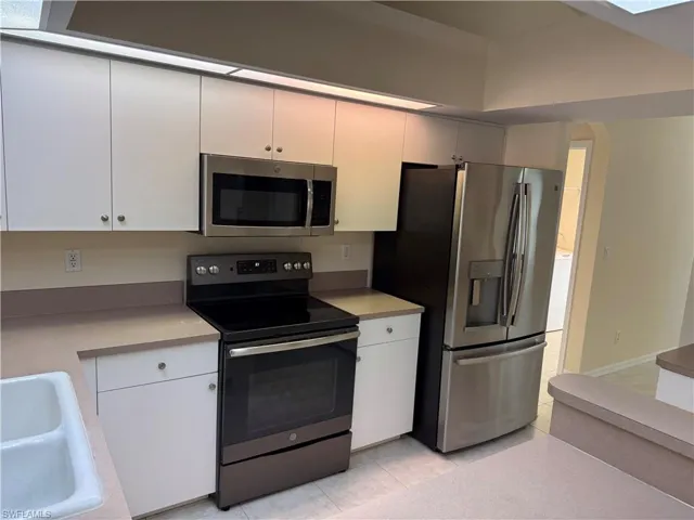 Kitchen featuring appliances with stainless steel finishes, light tile patterned flooring, light countertops, and white cabinets