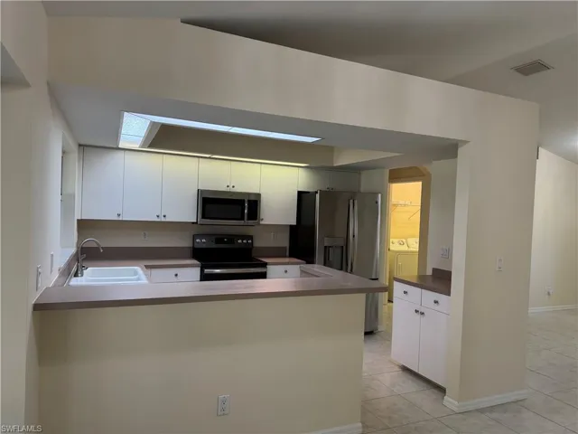 Kitchen with a peninsula, white cabinetry, appliances with stainless steel finishes, and washer and dryer