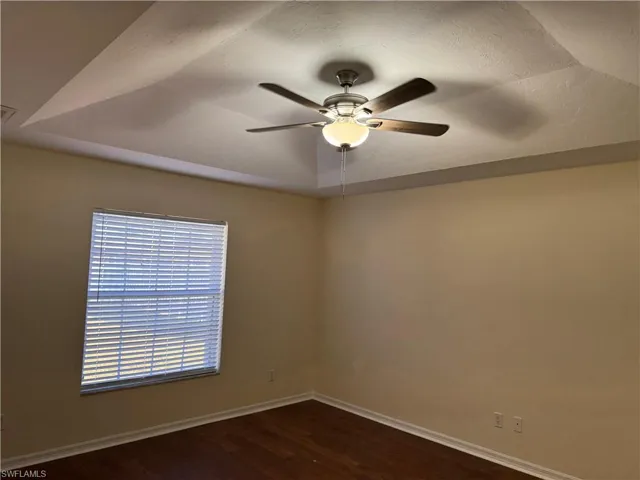 Unfurnished room featuring dark wood-type flooring, a ceiling fan, and a tray ceiling