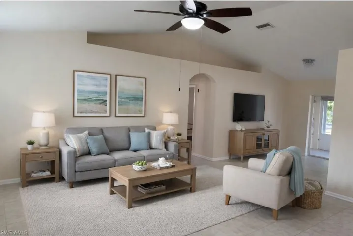 Living room with arched walkways, ceiling fan, vaulted ceiling, and light tile patterned floors