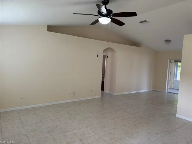 Empty room with lofted ceiling, arched walkways, ceiling fan, and light tile patterned floors