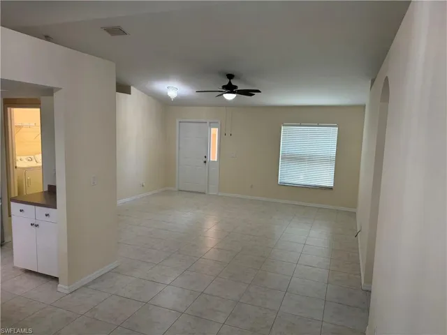 Empty room featuring a ceiling fan, washer / clothes dryer, arched walkways, and light tile patterned flooring