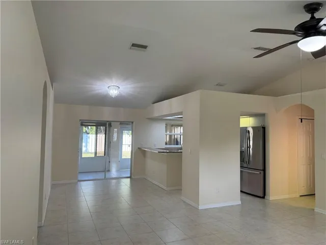 Empty room featuring arched walkways, vaulted ceiling, a ceiling fan, and light tile patterned floors