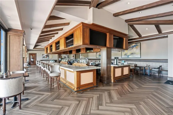 Vineyards Country Club - Pub featuring herringbone wood-finish flooring, exposed ceiling beams, built-in bar with stone countertop, wood paneling, and recessed lighting