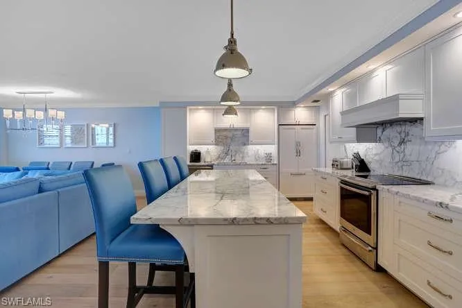 Kitchen with stainless steel electric range oven, a center island, paneled refrigerator, natural hardwood wood floors, and decorative light fixtures