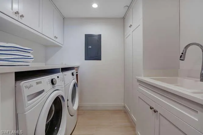 Washroom with cabinets, electric panel, sink, washing machine and dryer, and  wood flooring