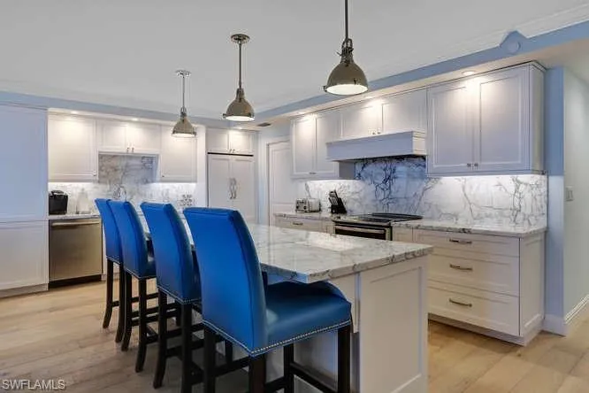 Kitchen with marble countertops and backsplash, appliances with stainless steel , pendant lighting, a kitchen island, and light wood floors