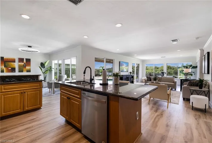 Kitchen with open floor plan, brown cabinets, dishwasher, dark stone countertops, and light wood finished floors