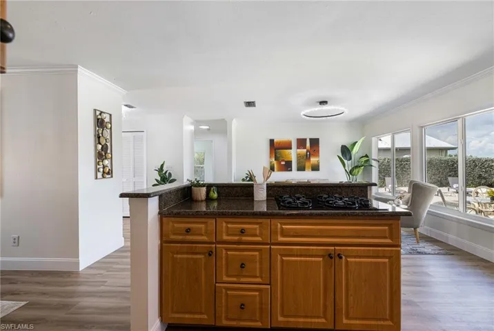 Kitchen featuring brown cabinetry, a center island, dark wood finished floors, crown molding, and black gas stovetop