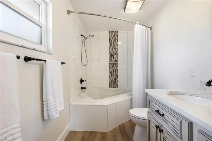 Full bathroom with tiled shower / bath combo, dark wood-style floors, and vanity