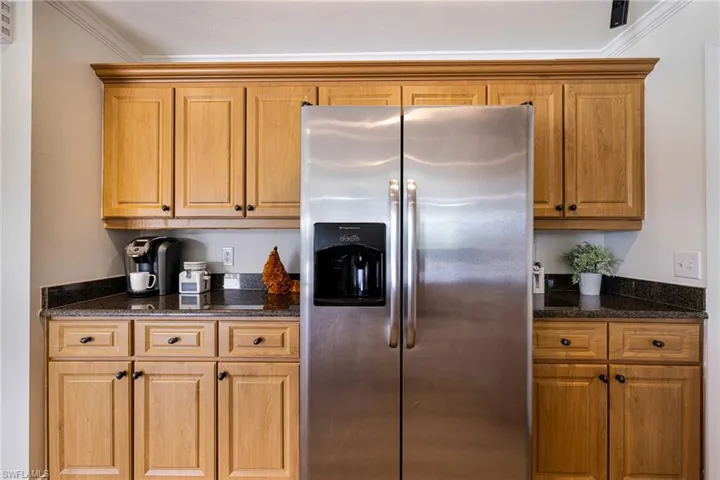 Kitchen featuring stainless steel fridge with ice dispenser, dark stone counters, crown molding, and brown cabinets