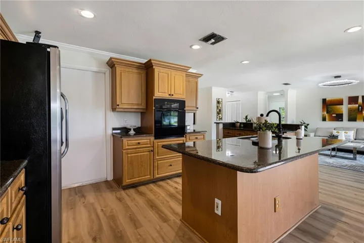 Kitchen with freestanding refrigerator, dark stone countertops, light wood finished floors, recessed lighting, and brown cabinetry